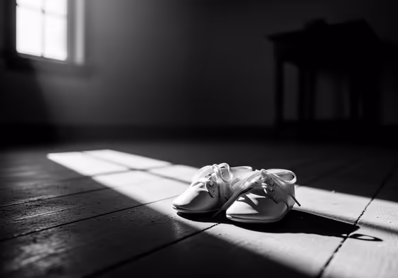 A poignant black and white photo of a single pair of tiny, unused baby shoes sitting alone in a dimly lit room.