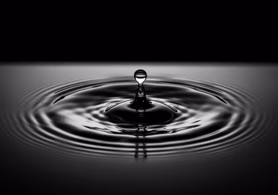 A minimalist, high-contrast image of a single teardrop hitting a dark, still surface of water, creating expanding ripples.